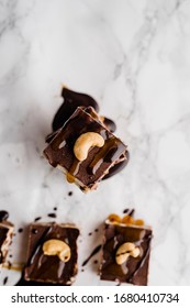 Close-up Directly Above Of A Vegan No-bake Chocolate Date And Coconut Healthy Bites With Peanutbutter And Syrup With A Cashew Nut On Top On White Marble