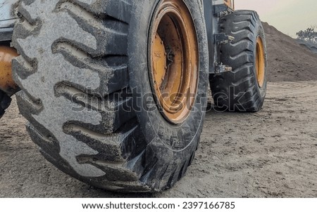  Close-up of a dirty loader wheel with a large tread , Detail on tire track pattern on a yellow heavy duty digger excavator on a dark soil