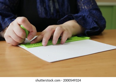 Close-up Of Disability Blind Person Woman Hands Writing Braille Text On Paper By Using Slate And Stylus Tools Making Embossed Printing For Braille Character Encoding. 