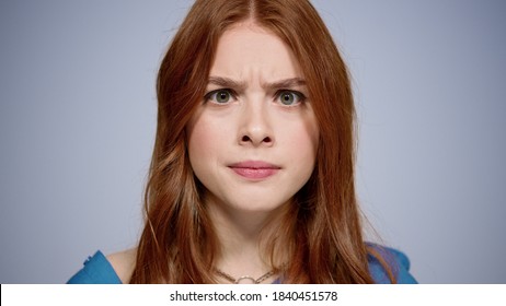 Closeup Disappointed Red Hair Woman Staring At Lens On Gray Background. Portrait Of Apathetic Female Person Posing Indoors. Confused Girl Looking At Camera In Studio.