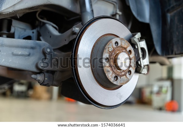 Closeup disc\
brake of the vehicle damaged , in process of new tire replacement.\
Car brake repairing in\
garage