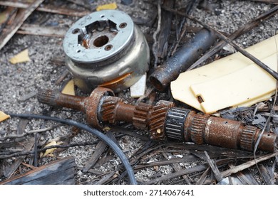 Close-up of discarded mechanical components, rusty gears, and wires scattered on a gravel surface.