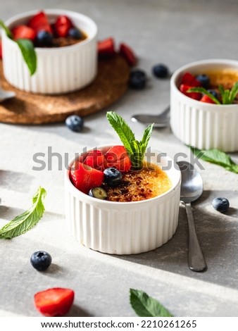 close-up of the crème brulée in soufflé dishes with fresh strawberries, blueberries and mint leaves with hard shadows