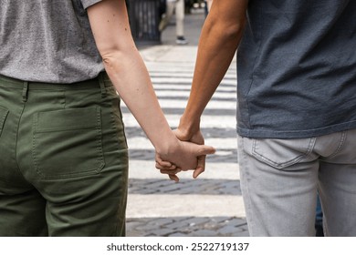 Close-up of diverse couple holding hands while crossing street. Interracial relationship, unity and love concept. Urban setting with pedestrian crossing in background. - Powered by Shutterstock