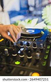 Close-up of DJ hand adjusting knobs on mixer with vibrant LED lights, turntable and sound equipment, capturing the energy of live music performance.