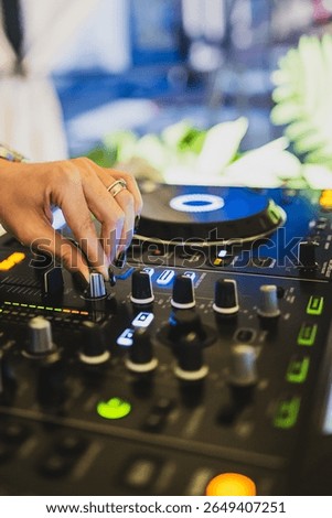 Close-up of DJ hand adjusting knobs on mixer with vibrant LED lights, turntable and sound equipment, capturing the energy of live music performance.