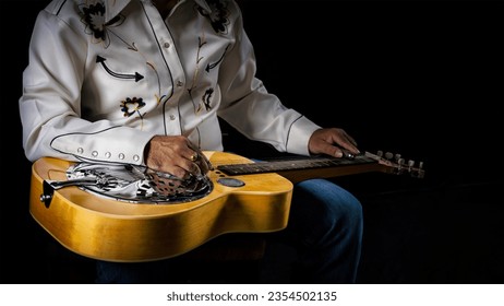 Close-up of a Dobro guitar resting on the lap of a musician dressed in cowboy attire on a dark backdrop - Powered by Shutterstock