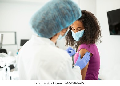 Close-up of a doctor administering a vaccine injection into a patient's arm. The patient is wearing a purple shirt, and the doctor's gloved hands are holding the syringe. - Powered by Shutterstock