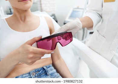 Closeup Of Doctor Aesthetician Hands Bringing Protective UV Goggles To Client During Visit For Laser Hair Removal Procedure In SPA Clinic. Skin And Body Care Concept