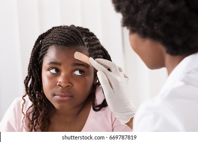 Close-up Of A Doctor Applying Band Aid To Girl Head In Clinic