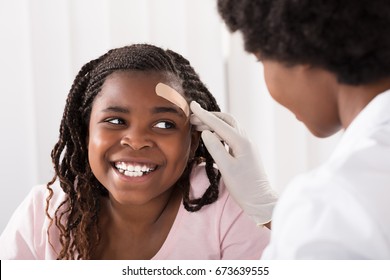 Close-up Of A Doctor Applying Band Aid To Girl Head In Clinic