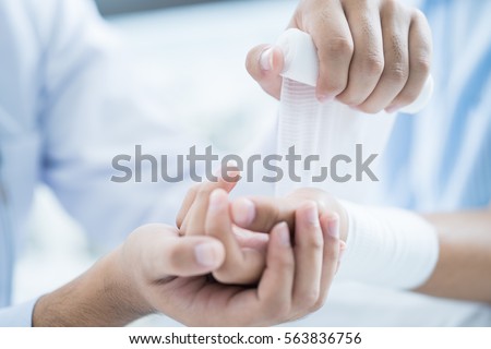 Close-up doctor is bandaging upper limb of patient.