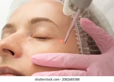 close-up Doctor cosmetologist makes the procedure of laser dermal rejuvenation of the eyelids of the skin around the eyes to the patient. Against the background of a medical office with copy space.