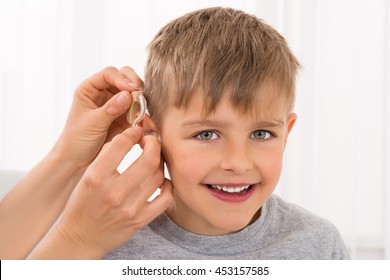 Close-up Of A Doctor Fitting Hearing Aid On Smiling Boy's Ear