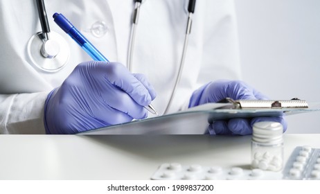 Close-up of doctor hands writing prescription in medical record on tablet.Doctor in white coat and blue gloves holds pills in his hands and writes prescription with blue pen.Medical banner concept