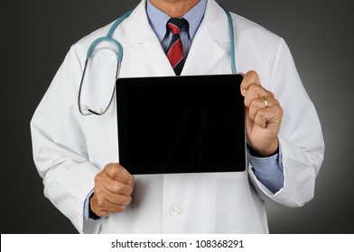 Closeup Of A Doctor Holding A Tablet Computer With A Blank Black Screen In Front Of His Torso.  Horizontal Format Over A Light To Dark Gray Background. Man Is Unrecognizable.