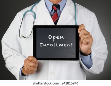 Closeup of a doctor holding a tablet computer with a chalkboard screen with the words Open Enrollment. Man is unrecognizable. 