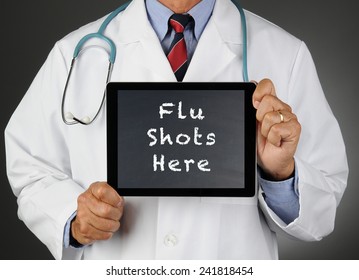 Closeup Of A Doctor Holding A Tablet Computer With A Chalkboard Screen With The Words Flu Shots Here. Man Is Unrecognizable.