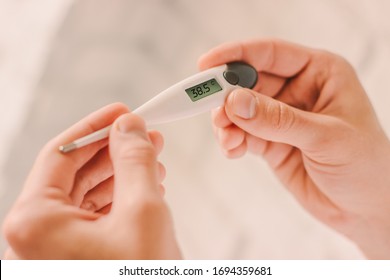 Closeup doctor looking at electronic thermometer with high fever body temperature in hospital. Sick man patient holding digital thermometer in hands. Diagnosis and test coronavirus COVID-19 symptoms