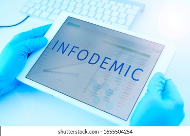 closeup of a doctor man, wearing blue surgical gloves, having a digital tablet in his hands with the word infodemic in its screen