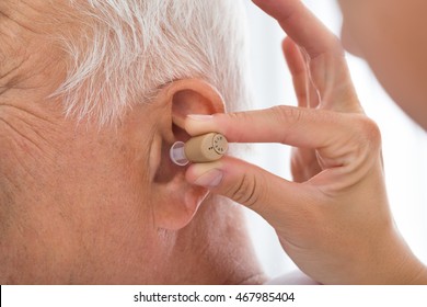 Close-up Of Doctor Putting Hearing Aid In Senior Patient's Ear