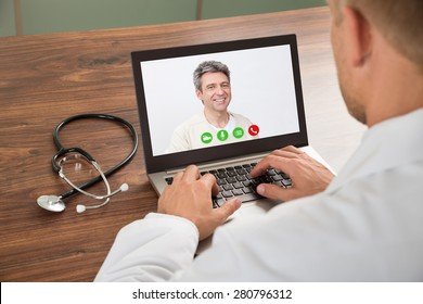 Close-up Of Doctor Talking To Male Patient Through Video Chat On Laptop At Desk