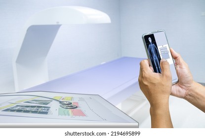 Close-up Doctor Uses A Smartphone To Check An Image Of A DXA Bone Density Scan On A Monitor In A Woman To Prevent Osteoporosis. Blurry Bone Densitometer Machine Background.Medical Technology Concept.