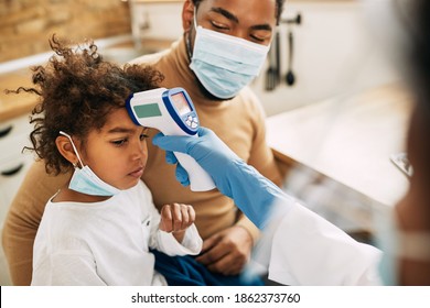 Close-up Of A Doctor Visiting Family At Home And Measuring Girl's Temperature With Infrared Thermometer Due To Coronavirus Pandemic. 