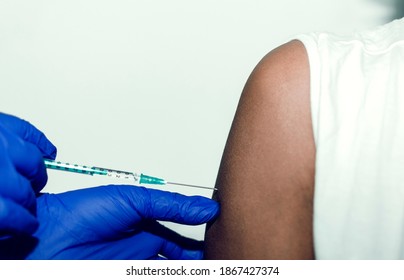 Closeup Of A Doctor Wearing Blue Gloves Injecting A Syringe In A Black Woman's Arm.  Covid-19 Vaccine. Selective Focus On The Arm.