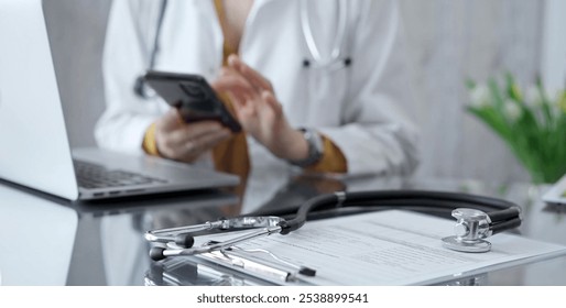 Close-up of doctor's desk with stethoscope and clipboard. Physician is using a tablet at the background. Medicine and health care - Powered by Shutterstock