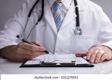 Close-up Of A Doctor's Hand Analyzing Report On White Desk