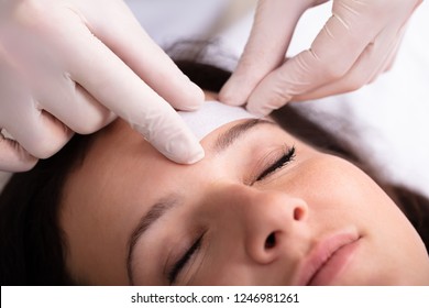 Close-up Of Doctor's Hand Waxing Woman's Forehead With Wax Strip