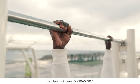 Close-up of doing pull-ups, man in white sportswear practicing outdoors in the evening, street workout, active lifestyle