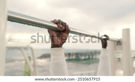 Close-up of doing pull-ups, man in white sportswear practicing outdoors in the evening, street workout, active lifestyle