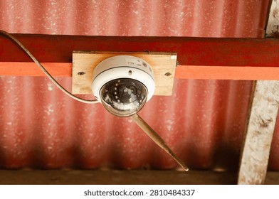 Close-up of a dome CCTV security camera mounted on a wooden ceiling inside a building. The surveillance device represents modern security systems, property protection, crime prevention, monitoring technology, and public safety.