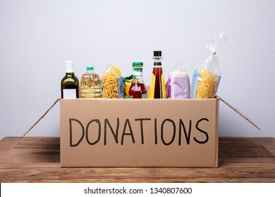 Close-up Of A Donation Box With Various Food Items On Wooden Desk