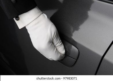 Closeup of a doorman or valet with his hand on the latch of a car door. 
