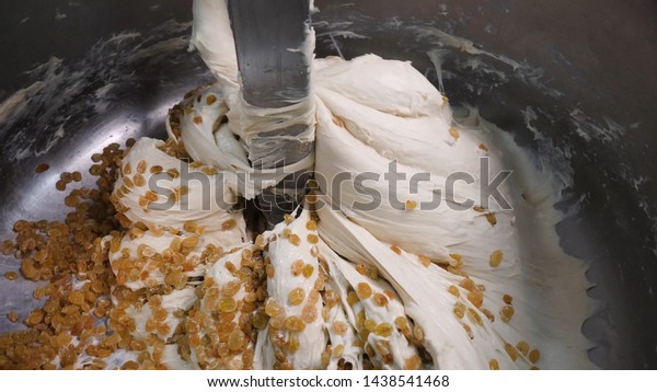 Close-up of dough with raisins in\
mixer. Stock footage. Delicious industrial pastries prepared for\
bakery. Large amount of raisins is mixed with yeast dough in\
stirrer