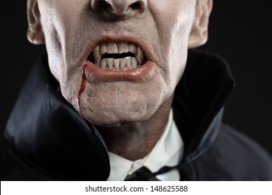 Close-up Of Dracula With Black Cape Showing His Scary Teeth. Vamp Fangs. Studio Shot Against Black.