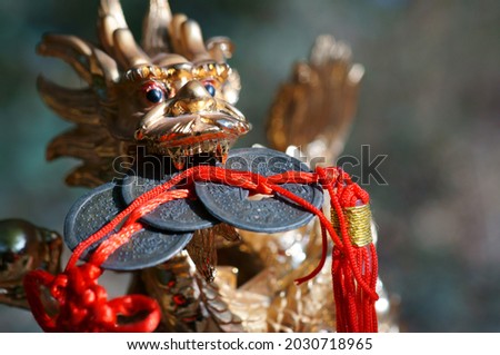 Close-up dragon figurine. In the dragon's teeth is a bunch of Chinese coins. Symbol of well-being and monetary prosperity.