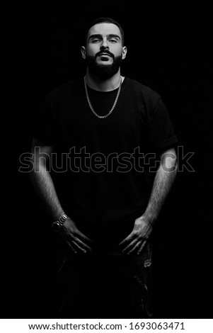 close-up of a dramatic portrait of a young serious guy, musician, singer, rapper with a beard in black clothes on a black isolated background. black and white photography.