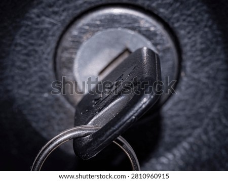 A close-up, dramatic shot of a black key inserted into a metallic ignition cylinder lock, typically found in a car or motorcycle