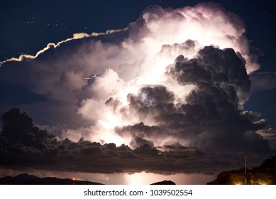 Close-up of dramatic thunderstorm with huge clouds and lightning over islands in the sea at night.