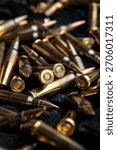 A close-up, dramatic view of brass and copper rifle ammunition piled on a dark textured surface.
