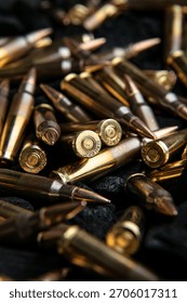 A close-up, dramatic view of brass and copper rifle ammunition piled on a dark textured surface.