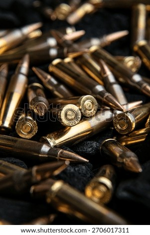 A close-up, dramatic view of brass and copper rifle ammunition piled on a dark textured surface.