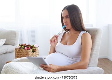 Closeup of dreaming pregnant woman writing baby names in notebook in armchair 