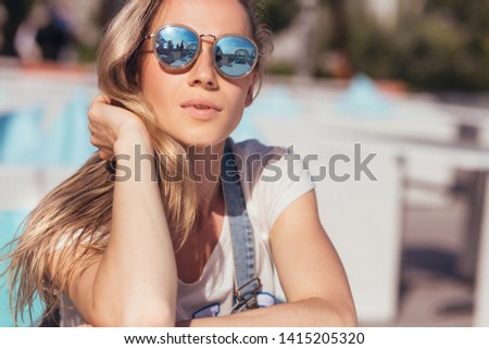 Close-up dreamy satisfied woman tourist in sunglasses smiling looking at camera on a sunny summer day while relaxing in the sun by the sea on a hot sunny day