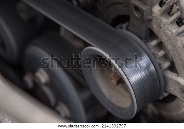 Close-up of the drive belt and the alternator\
roller in the car engine. Dirty\
motor