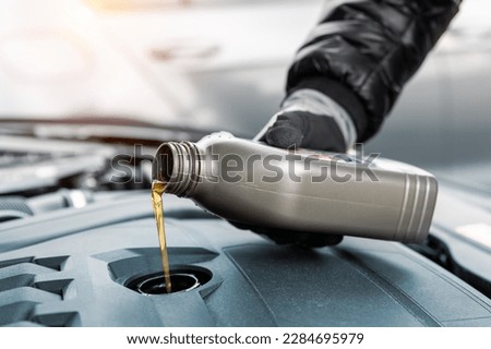 Close-up driver hand holding small bottle can pouring synthetic motor oil in diesel or petrol turbocharged vehicle engine due oil consumption. New lubricant diy change. Car service maintenance work
